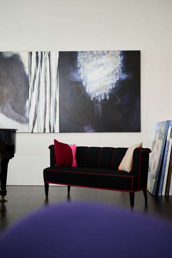 Zithoek met grote abstracte schilderijen van een kroonluchter en strepen boven een zwarte sofa met piano