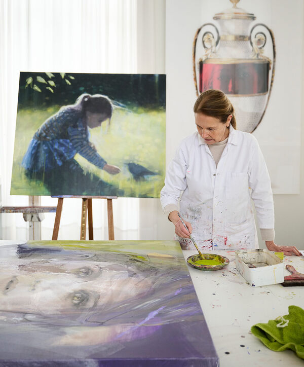Christine Comyn mengt verf in haar atelier, omringd door schilderijen en een groot vaas-kunstwerk